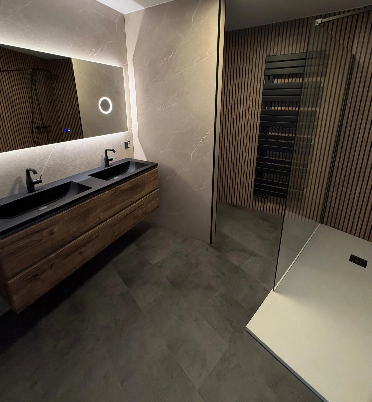 Badkamer met zwevend houten dubbel wastafelmeubel, zwarte wastafels, ledspiegel en inloopdouche met houten lamellenwand