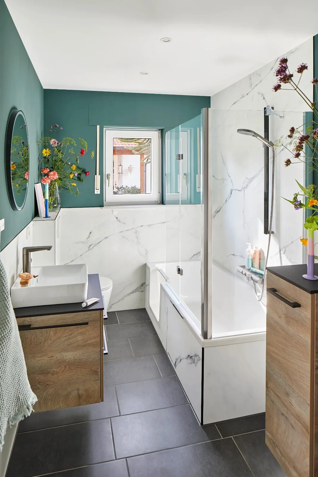 Badkamer met groene wand, marmerlook wanden, ligbad met glazen scherm en houten wastafelmeubel