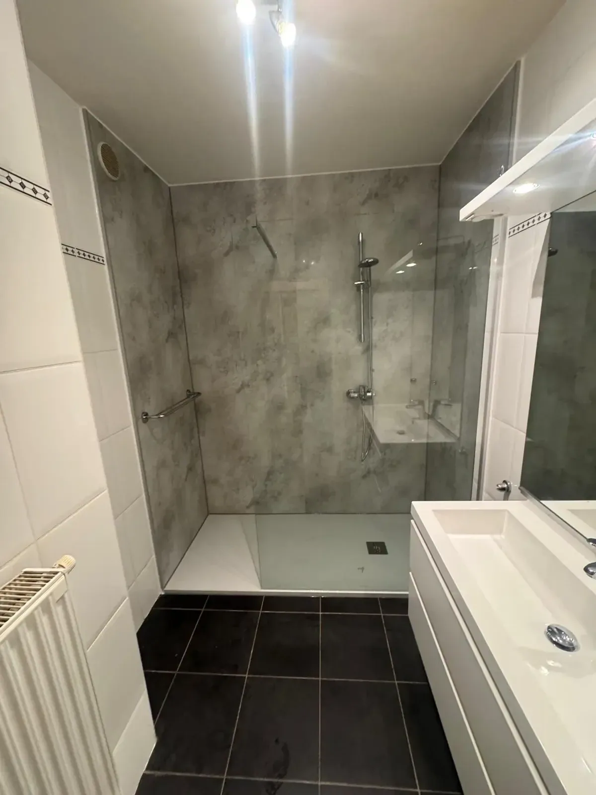 Badkamer met inloopdouche en grijze marmerlook wandpanelen, wit wastafelmeubel en donkere vloertegels