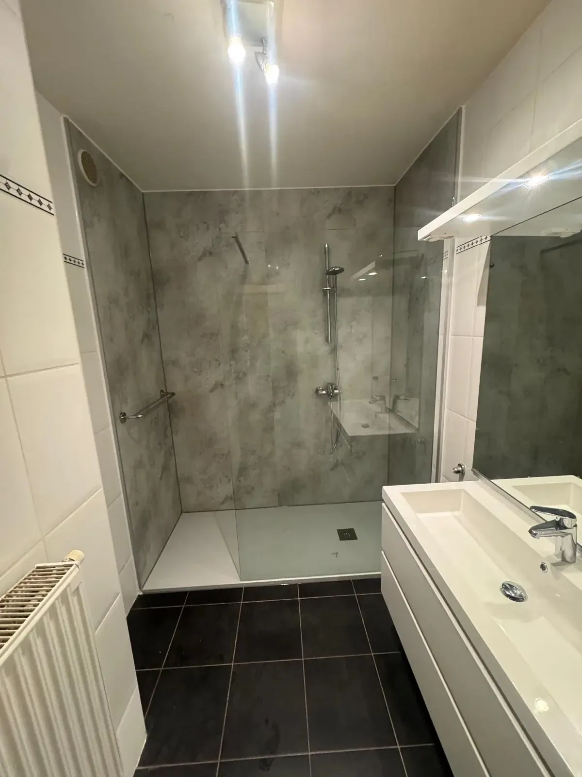 Badkamer met inloopdouche, grijze marmerlook wandpanelen, wit wastafelmeubel en donkere vloer