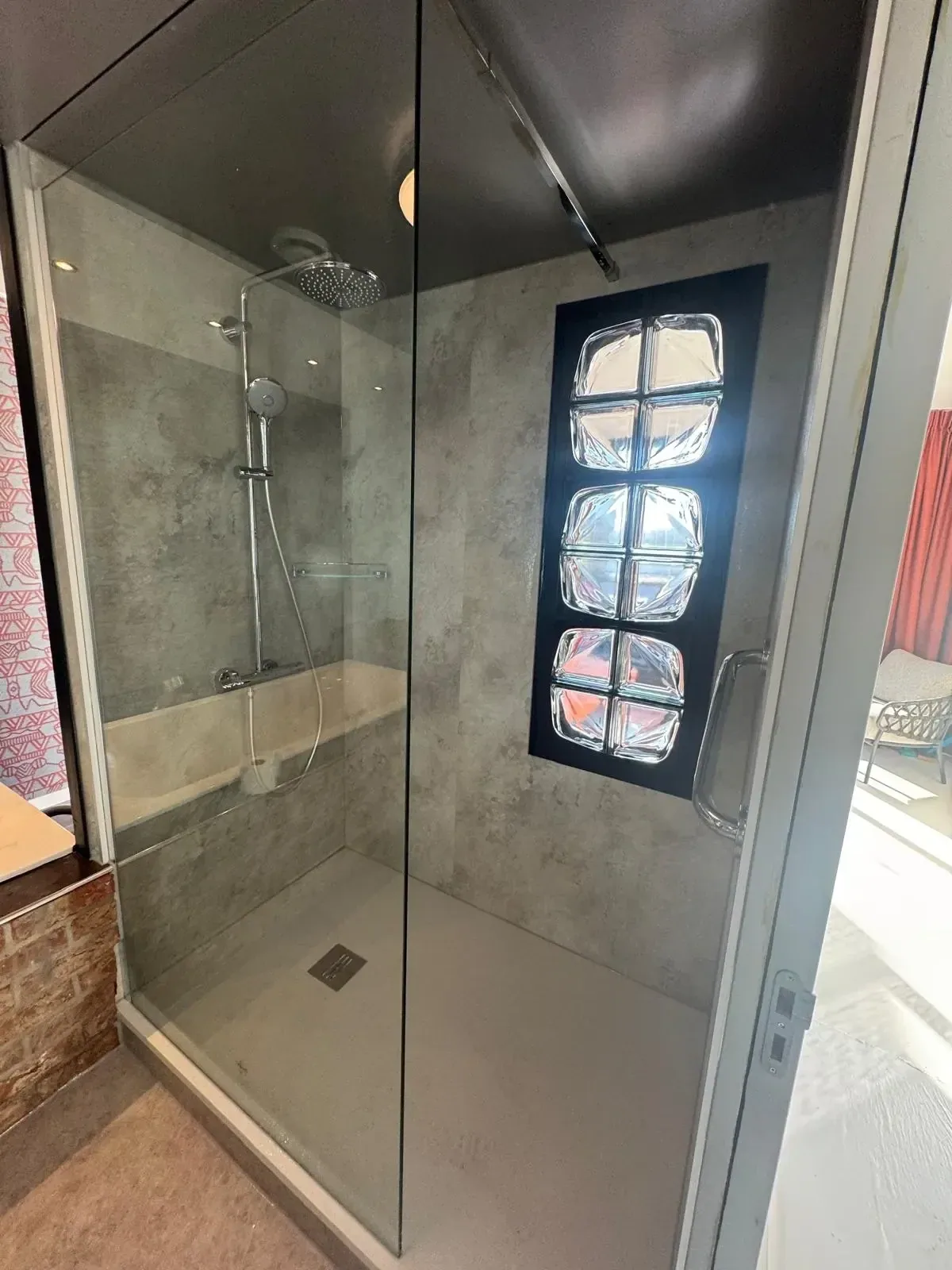 Douche met betonlook wandpanelen, regendouche en glasblokraam, glazen deur open