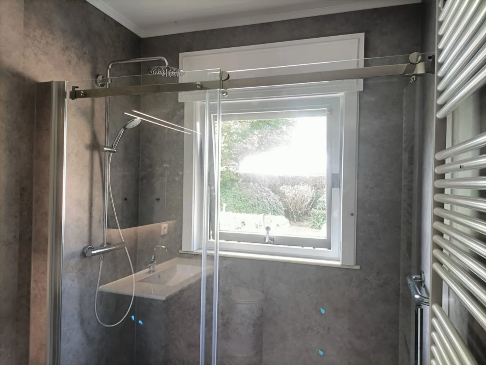 Douche met glazen schuifdeur, regendouche en grijze steenlook wandpanelen voor een raam