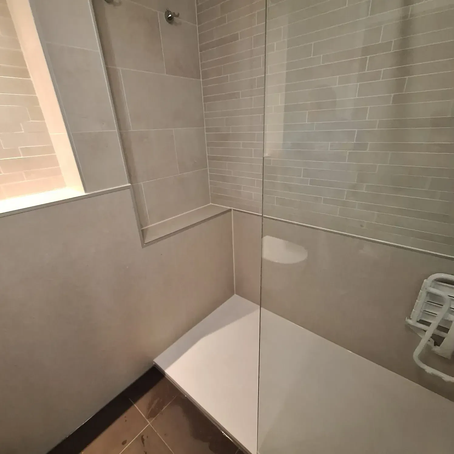 Douchehoek met lichte steenstrip-look wandpanelen, witte douchebak en glazen wand onder schuin dak