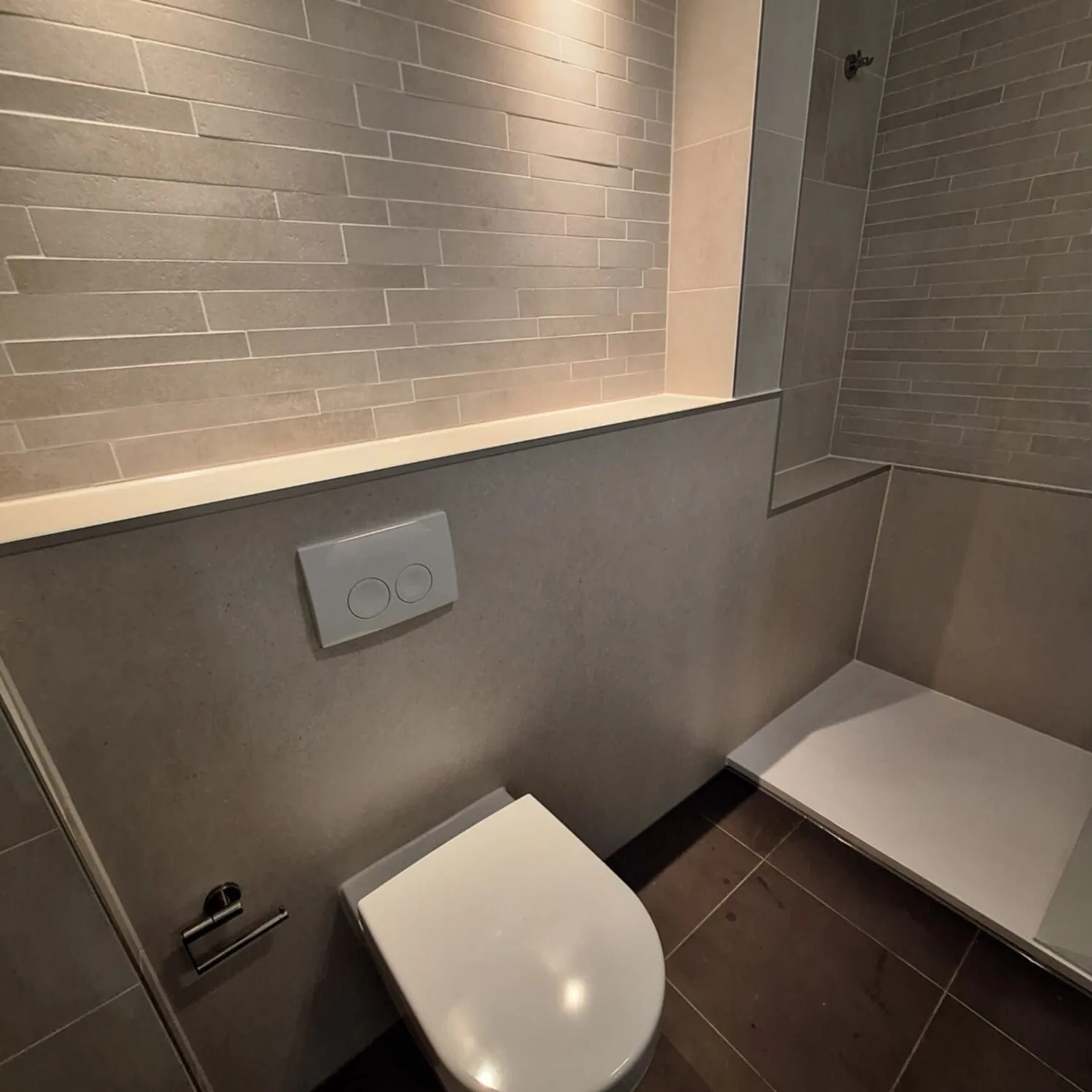 Hangtoilet tegen grijze voorzetwand met verlichte nis, rechts een witte douchevloer