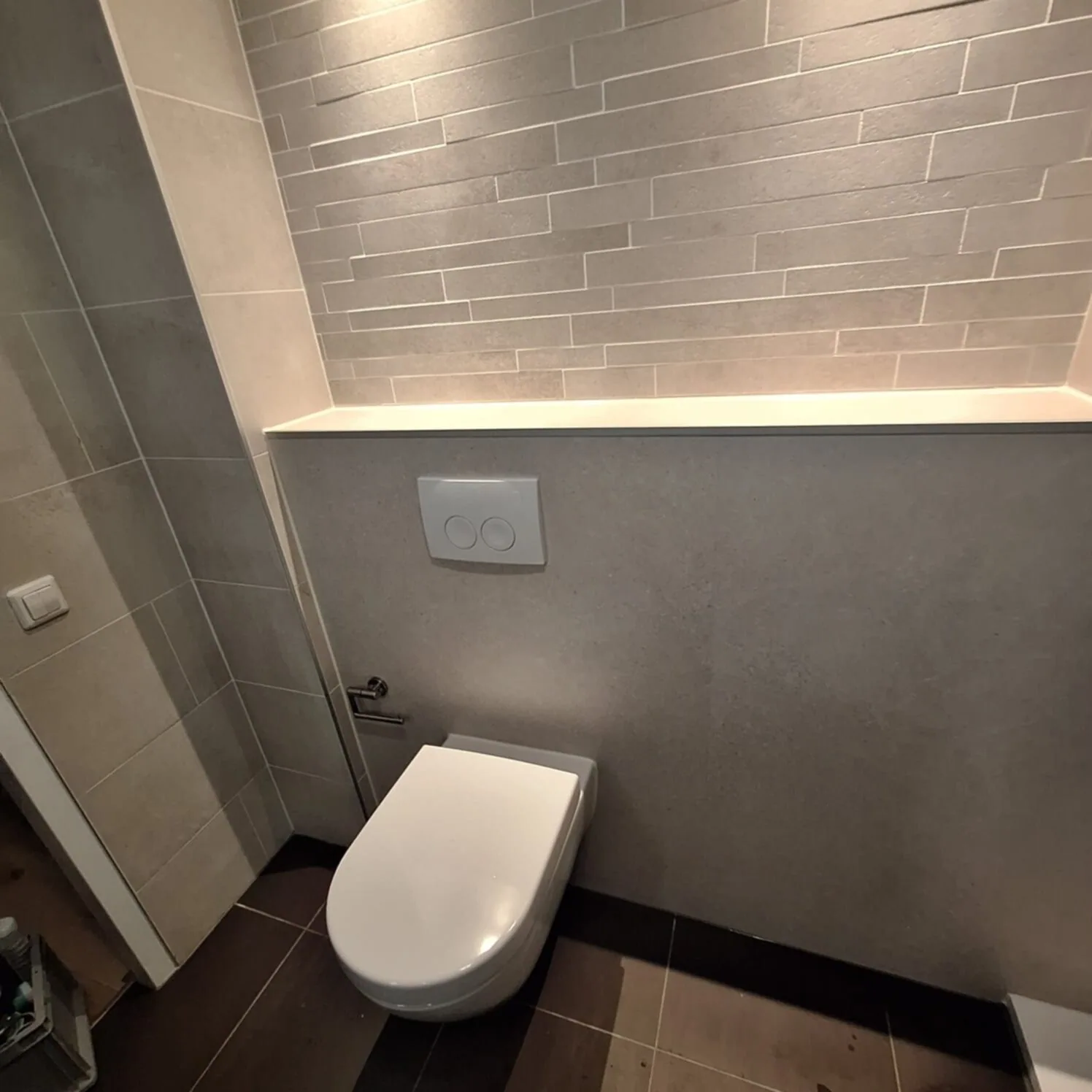 Hangtoilet tegen grijze voorzetwand met verlichte nis en strokenwand erboven