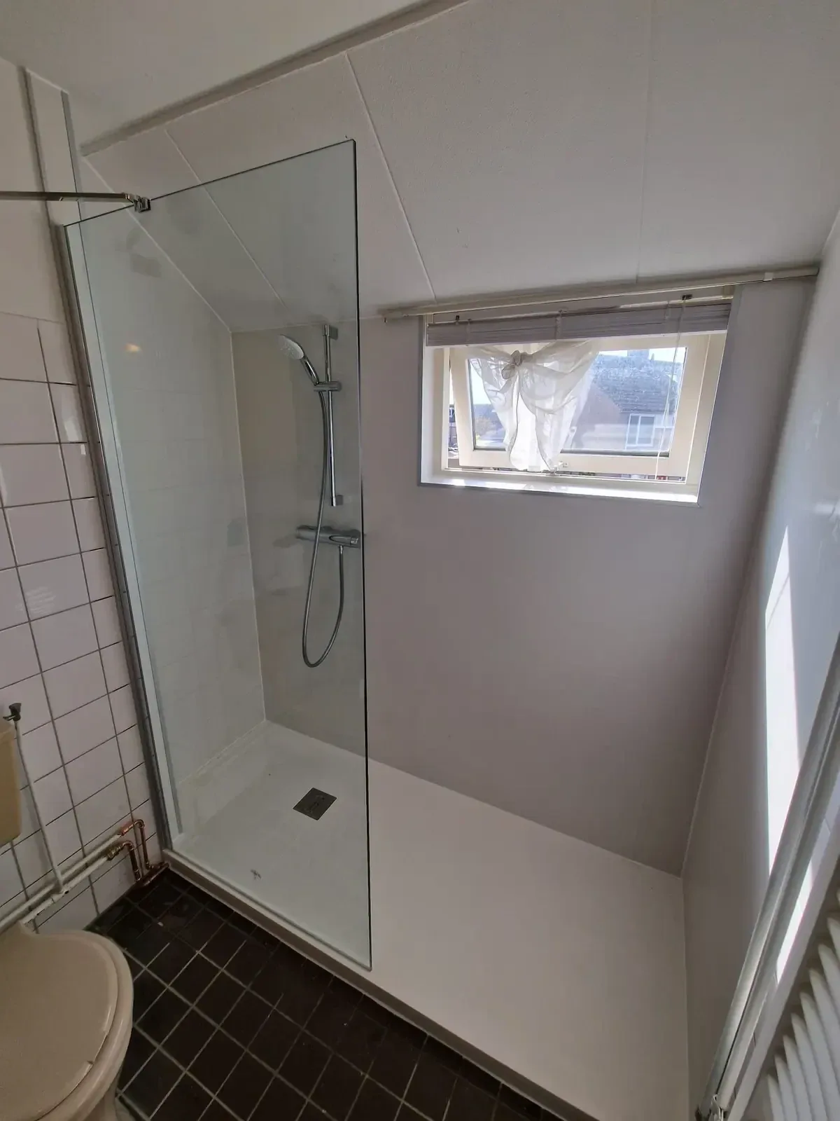 Inloopdouche onder schuin dak met glazen wand, witte douchevloer en raam