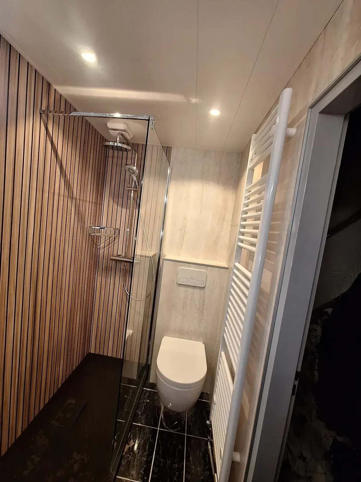 Smalle badkamer met houtlook lamellenwand, inloopdouche, hangtoilet en handdoekradiator