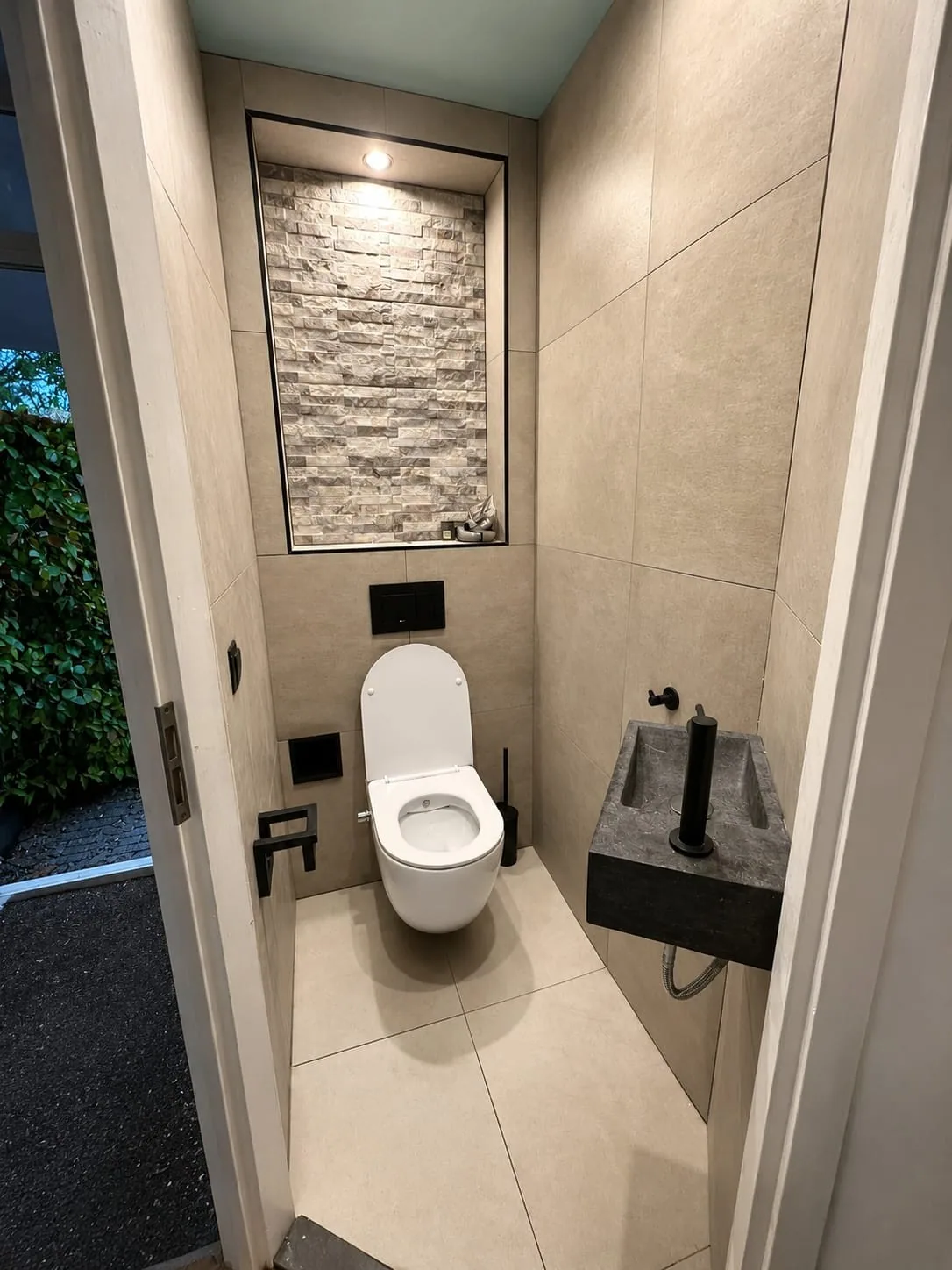 Toilet met hangtoilet, natuurstenen fonteintje en verlichte nis met steenstrips