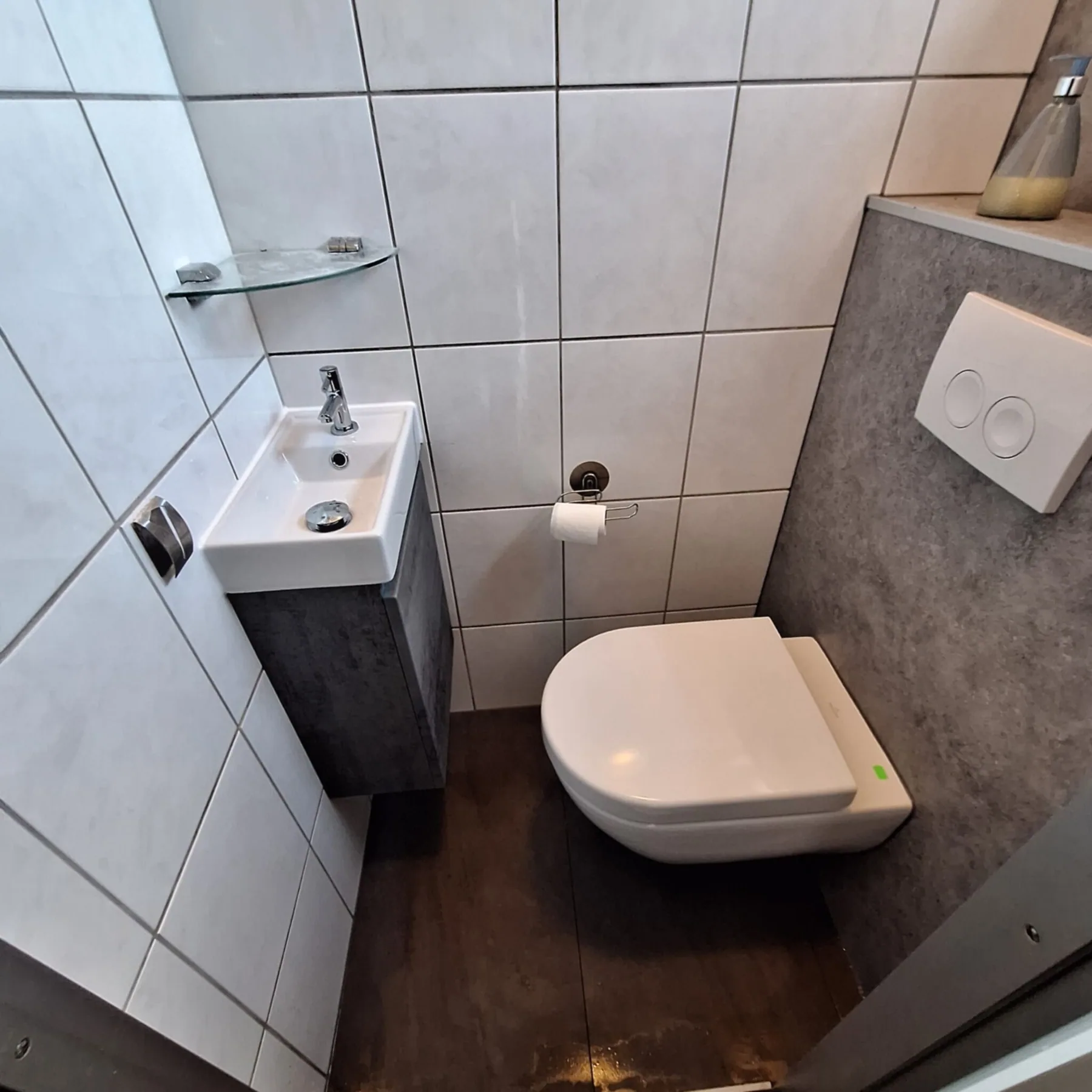 Klein toilet met hangtoilet, grijze voorzetwand met bedieningsplaat, fonteintje met meubel en houtlook vloer