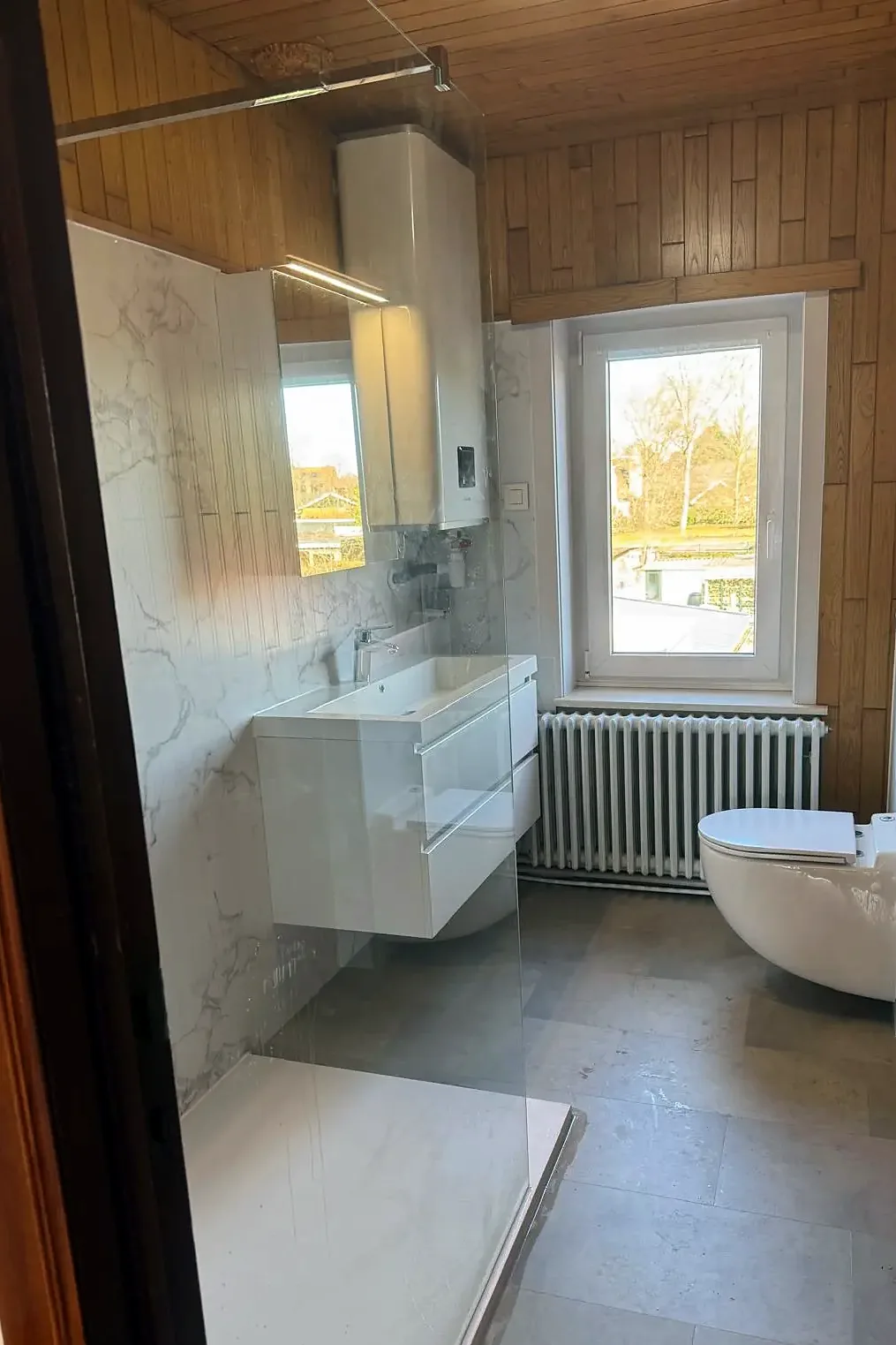 Na: dezelfde badkamer met lichte wandpanelen, wastafelmeubel en hangtoilet