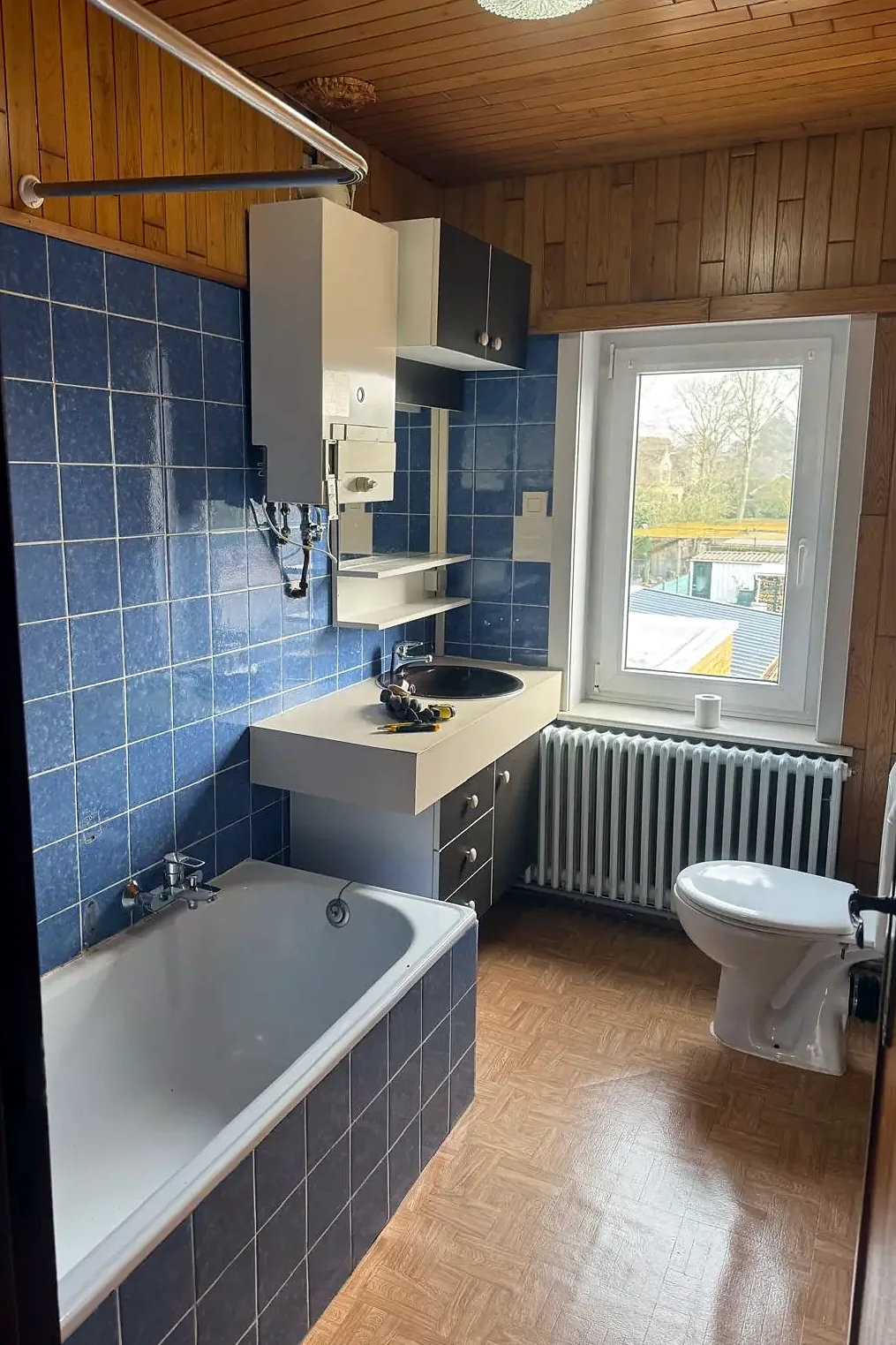Voor: badkamer met blauwe wandtegels, ligbad en staand toilet