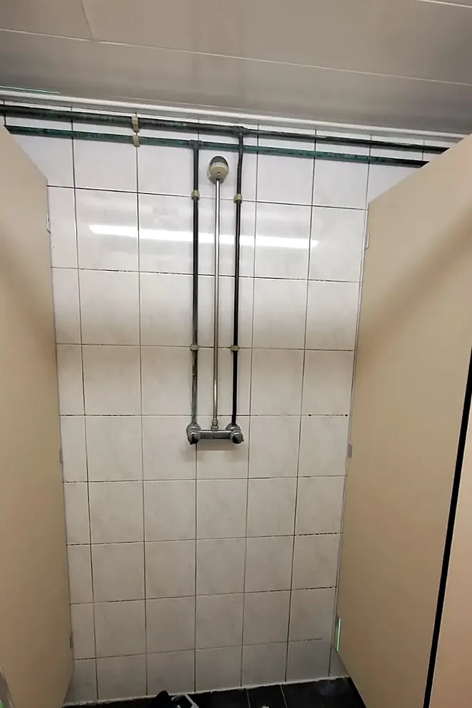 Voor: douche met witte wandtegels en opbouwleidingen