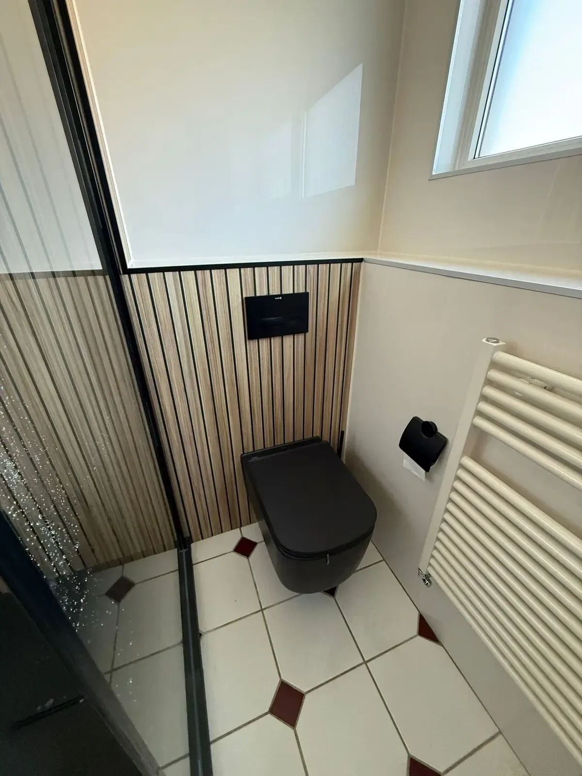 Zwart hangtoilet voor houtlook lamellen, handdoekradiator en tegelvloer met rode ruitjes